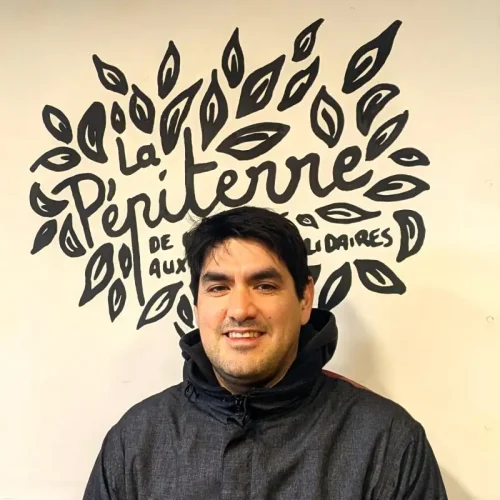 Homme souriant devant un mur avec le logo La Pepiterre, symbole d'engagement local et de produits du terroir.